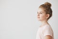 Close up of good-looking little girl with blonde hair in bun hairstyle, standing in three quarters, looking aside with