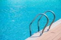 Close up grab bars ladder with blue water in swimming pool in the background.