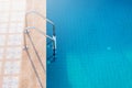 Close up grab bars ladder with blue water in swimming pool in the background.