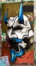Close up of a graffiti drawing of a white face mask with blue horns and red eyes.