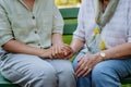 Close-up of granddaughter consoling her senior grandmother and touching her hand when sitting on bench in park in summer Royalty Free Stock Photo
