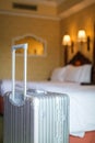 Close up gray silver travel suitcase is in an unoccupied hotel room and there is white linen cover.