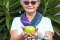 Close-up of a green apple in the hands of a senior smiling woman with scarf and sunglasses.  Concept of healthy eating and diet Royalty Free Stock Photo