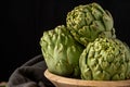 Close-up of green artichokes in wooden bowl and black cloth, with selective focus, black background, horizontal Royalty Free Stock Photo