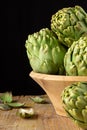 Close-up of green artichokes in wooden bowl, on wooden table, with selective focus, black background, vertical Royalty Free Stock Photo