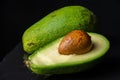 Close-up of green avocado cut in half with seed, on wet slate stone and black background Royalty Free Stock Photo