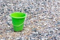 Close up of Green bucket or pail on the seashore sitting empty in the rocky sand next to the lake with blue water in background Royalty Free Stock Photo