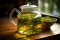 close-up of green herbal tea steeping inside a glass teapot on a wooden table