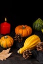 Close-up of green and orange pumpkins, with autumn leaves, pine cones and burning orange candle, selective focus, on dark wooden t Royalty Free Stock Photo