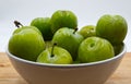 Close up of green plums fruit in a ceramic jar. Wooden table, white background