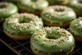 Close-up of green tea matcha doughnuts covered with green matcha powder icing and grated pistachio on a cooling rack, matcha