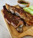 Close up Grilled pork ribs, sliced cucumber and spicy sauce on wooden tray. Barbecue food with fresh vegetables on white marble. Royalty Free Stock Photo