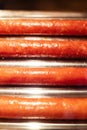 Close-up of grilled sausages in a cafe, which are fried to a brown crust. Cooking ingredients for a hot dog. Vertical photo