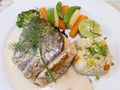 Close-up grilled sea bass steak served with white wine sauce, fried rice with butter, and cooked vegetables on white plate. Royalty Free Stock Photo