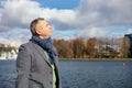 Close up grizzled mature retire man with eyeglasses on head in jacket and scarf stand near river and breath fresh air