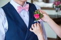 Close-up of groom in blue suit pinning a pink rose boutonniere to a jacket in the room.