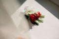 Close-up the groom`s buttonhole white and red flowers and green and greenery lying on the table. Bride`s Preparations