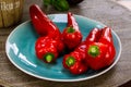 Close up of group of isolated long red bell peppers on blue china dish and round wood table. Blurred basil pot background Royalty Free Stock Photo