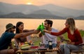 Close up group of multi-ethnic friends men and women sit on chair with party and camping together also cheers with bottle near