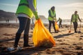 Close Up Of Group Of Volunteers Clearing Trash From Beach And Putting It Into Bags