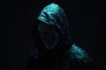 Close-up of a hacker with a glowing face wearing black hood on dark background. Royalty Free Stock Photo
