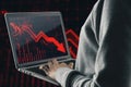 Close up of hacker hands using laptop with red candlestick arrow going down on blurry background. Economic recession and crisis