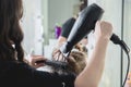 Close up of hairdressers hands drying long blond hair with blow dryer and round brush