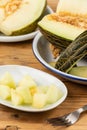 Close-up of half a green melon, plate with pieces and fork on wooden table Royalty Free Stock Photo