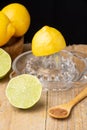 Close-up of half a lemon on glass juicer, limes, wooden spoon with brown sugar, wooden bowl with lemons, black background