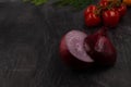 Close-up of a halved head of purple onion against a dark metal background with cherry tomatoes behind