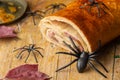 Close-up of ham bread for halloween on wooden table with plastic spiders, selective focus