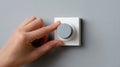 Close-up of hand adjusting modern gray rotary dimmer switch on light gray wall in minimalistic interior setting Royalty Free Stock Photo