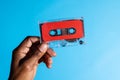 Close up of hand of african american man holding red cassette tape over blue background Royalty Free Stock Photo