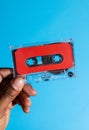 Close up of hand of african american man holding red cassette tape over blue background Royalty Free Stock Photo