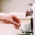 Close up of hand of barista brewing coffee using a coffee machine. The man is standing and holding a white cup Royalty Free Stock Photo