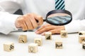 Close up hand of businessperson looking at wooden blocks with various icon symbols through magnifying glass.