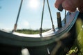 Close-up of a hand with a cap from a nipple on a bicycle wheel, in a meadow, against the background of the sky. Flat Royalty Free Stock Photo