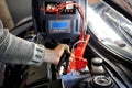 Close up of hand charging car battery with electricity trough jumper cables on the background of the charger Royalty Free Stock Photo