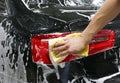 Close-up of hand cleaning black car of serviceman. The process of washing cars with foam and sponge. Royalty Free Stock Photo