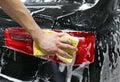 Close-up of hand cleaning black car of serviceman. The process of washing cars with foam and sponge. Royalty Free Stock Photo