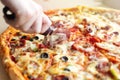 Close up of hand cutting large cheesy pepperoni pizza, background macro
