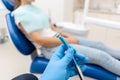 Close-up hand of dentist in the glove holds dental high speed turbine. The patient in blue chair at the background Royalty Free Stock Photo