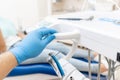 Close-up hand of dentist in the glove holds dental high speed turbine. The patient in blue chair at the background Royalty Free Stock Photo