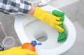 Close up hand with detergent cleaning toilet bowl in bathroom. Man in yellow rubber gloves cleaning toilet seat with green cloth. Royalty Free Stock Photo