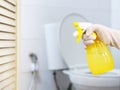 Close up hand with glove holding yellow spray bottle of cleanser over blurry white toilet background Royalty Free Stock Photo