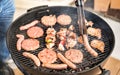 Close up of hand grilling meat at barbecue session - Skewers and burger sausages cooked on ember at bbq garden party - Pic nic Royalty Free Stock Photo