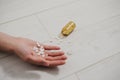 Close-up of a hand with a handful of pills in the palm, lying lifeless on the floor. Nearby is a bottle of pills. The consequences