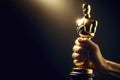 Close up hand hold gold oscar statue isolated on solid black background. ai generative