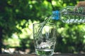 Close up hand holding bottle to pour water in the glass on nature and the sky background. Royalty Free Stock Photo