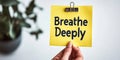Close-Up of Hand Holding Bright Yellow Sticky Note with the Reminder Breathe Deeply. Royalty Free Stock Photo